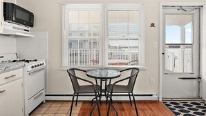 A kitchen with a stove, microwave, and two chairs at a table near a window with blinds. - Bayfront Condo with Great Location in Ocean City (Ocean City)