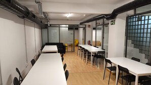 A conference room with white tables and black chairs, glass walls, and a fire extinguisher. - Beddy Hostels (Madrid)