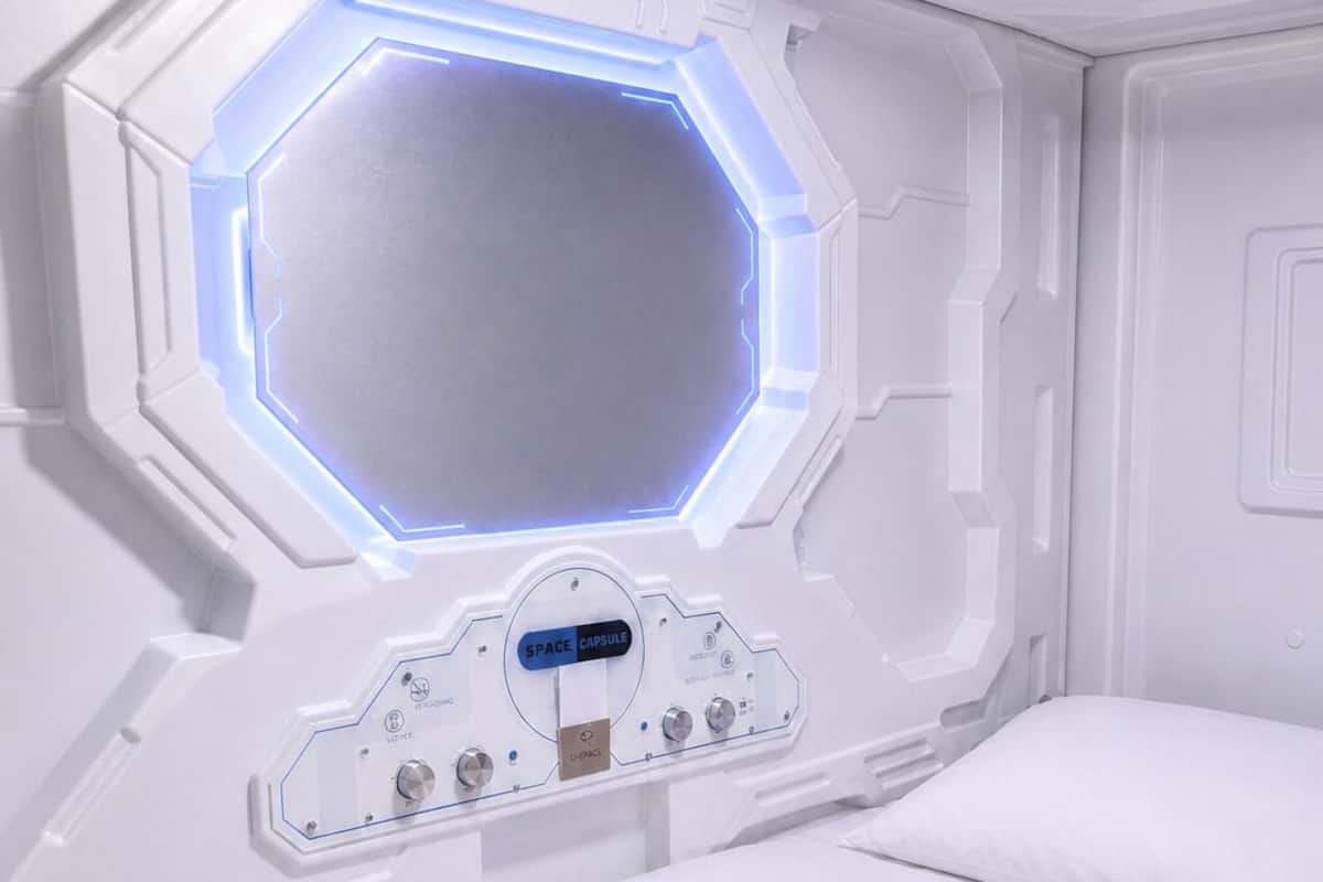 A room with a hexagonal window, a control panel with buttons, and two beds.