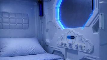 Una habitación con una cama, un panel de control y una ventana hexagonal.