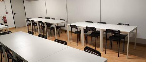 A conference room with multiple white tables and black chairs, a fire extinguisher, and a door labeled 'EXIT'.