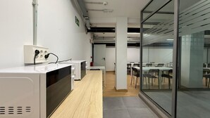 A modern office space with a long counter, multiple chairs, and a glass partition. - Beddy Hostels (Madrid)
