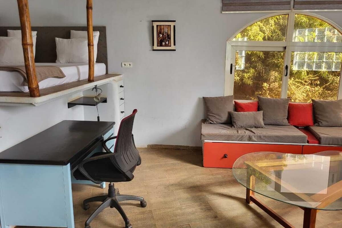 A room with a bed, a desk, a chair, a sofa, and a glass table.