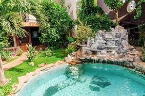 A swimming pool with a waterfall feature, surrounded by lush greenery and a small rock formation. - Hôtel Hacienda Ouagadougou (Ouagadougou)