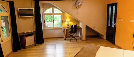 Una habitación con cama, escritorio, silla, televisor y ventana con cortinas.
