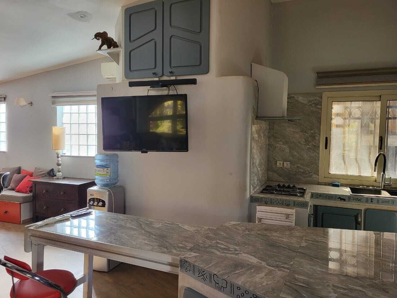 Una cocina con televisión integrada, dispensador de agua, estufa y comedor con mesa.