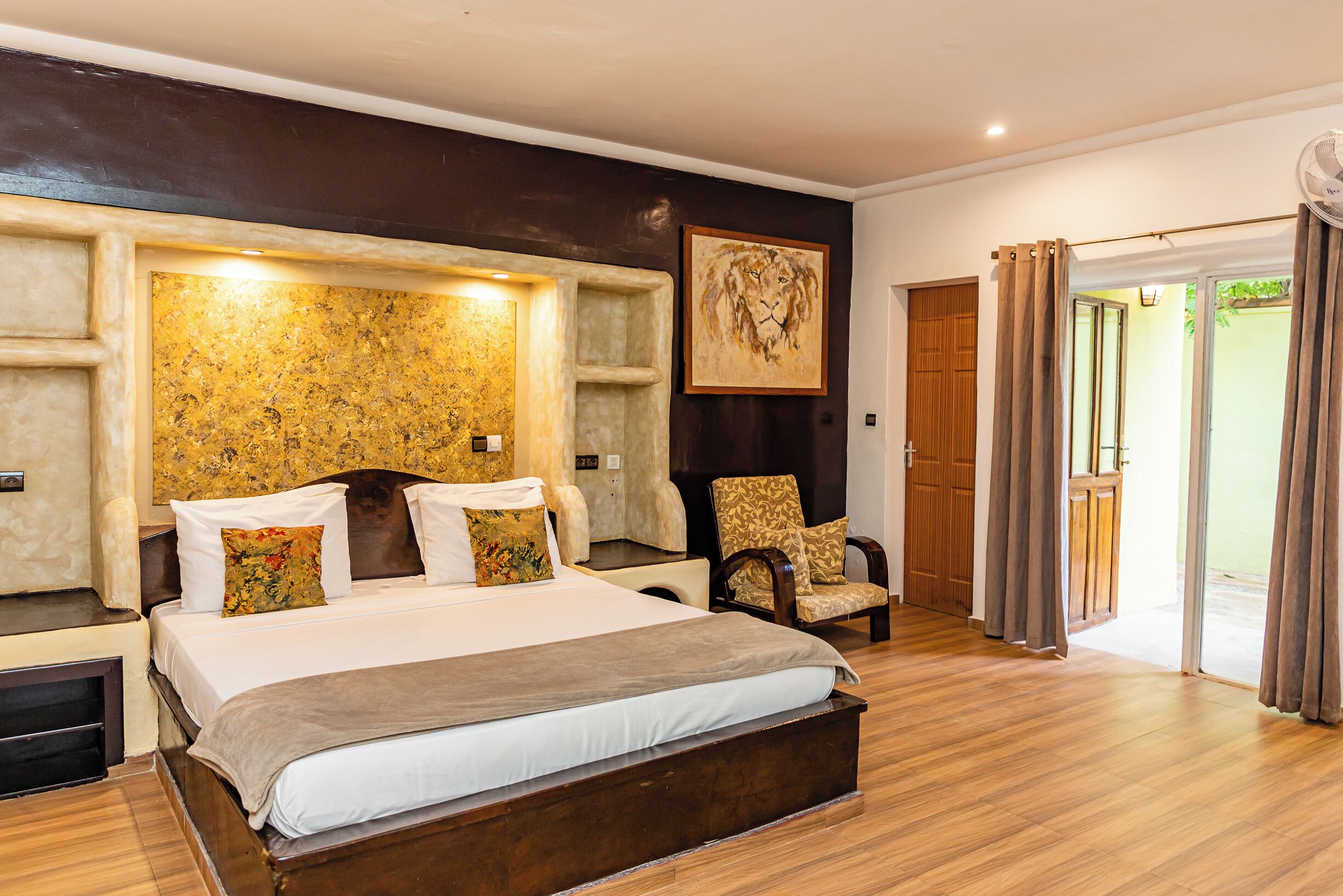 A spacious bedroom with a large bed, a wooden headboard, a chair, and a sliding glass door leading to an outdoor area.