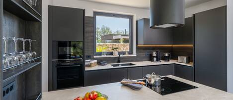 A modern kitchen with a large island, built-in appliances, and a window view.