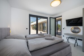 Ein modernes Schlafzimmer mit Schlafsofa, Wandfernseher und Blick ins Freie durch große Schiebetüren.