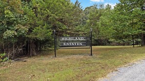 Un panneau indiquant l’emplacement de « Highland Estates », avec un cadre en métal et des lettres blanches, placé sur un fond de verdure composé d’arbres et d’herbe.