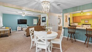 Un salon avec une table à manger blanche, un ventilateur de plafond et un lustre.