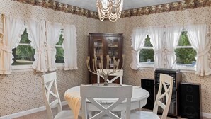 Un coin repas comprenant une table ronde, des chaises blanches, un lustre et un buffet aux portes vitrées.