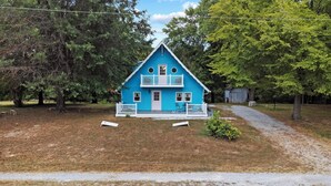 Une maison à deux étages, avec une façade bleue, un porche blanc et un petit jardin.