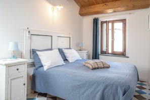 A bedroom with a bed, two bedside tables, a nightstand, a window with curtains, and a wooden ceiling. - The View House (Mondavio)