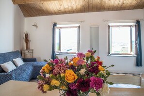 A room with a bed, a table with a vase of flowers, and two windows with curtains. - The View House (Mondavio)