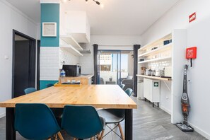 A modern kitchen with white cabinets, a wooden table, and blue chairs. - Apartment 'Rochanat - By Staywise' with Balcony, Wi-Fi, and Air Conditioning (Portimão)