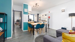 Een moderne woonkamer met een bank, een eethoek met stoelen en een tafel, een keuken met kasten, en een gang die naar een andere kamer leidt.