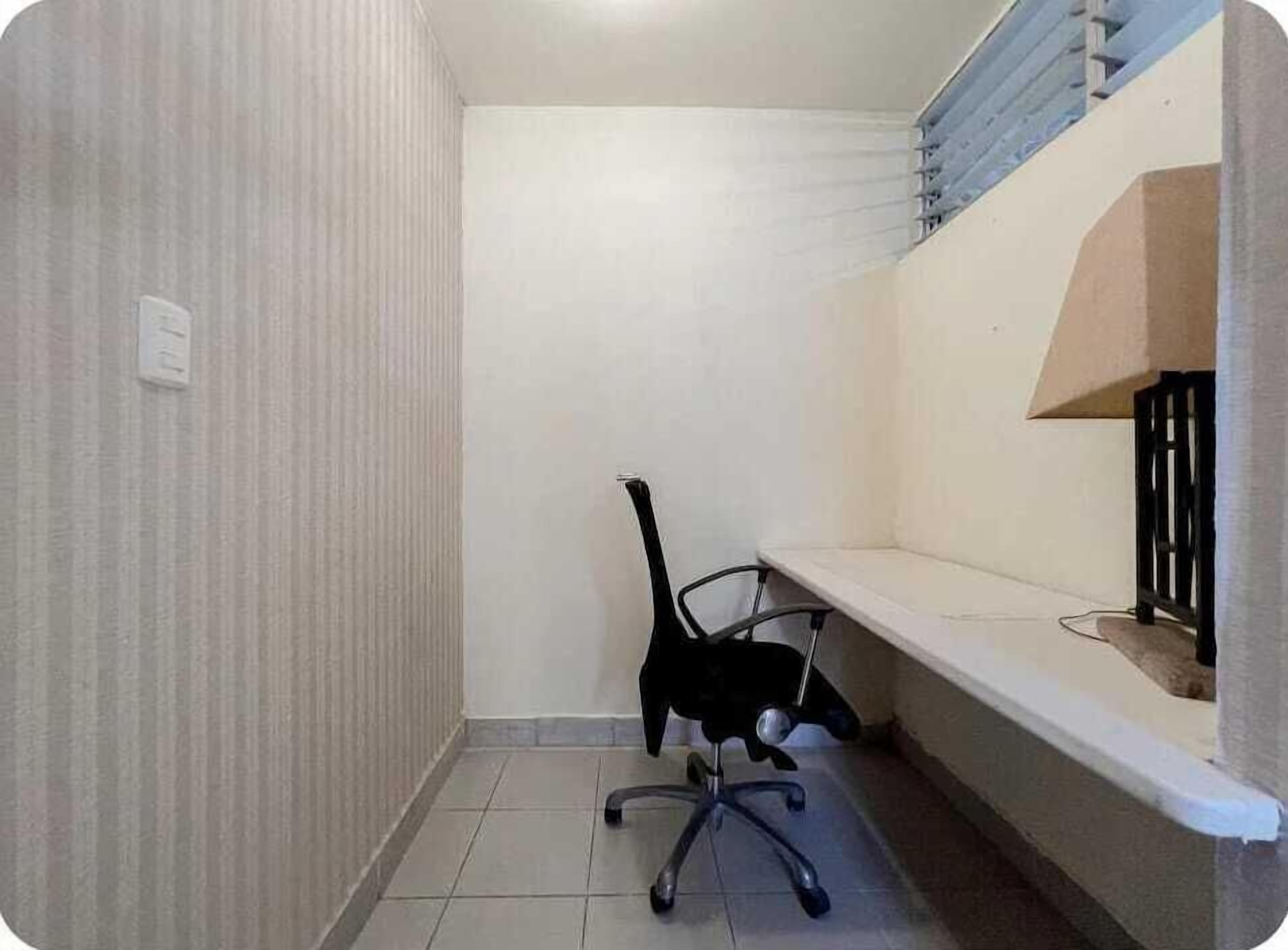 A small, clean room with a single black office chair, a white desk, and a white wall.