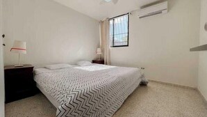 Ein Schlafzimmer mit Bett, Nachttisch, Lampe, Fenster und Deckenventilator.
