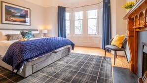 Ein Schlafzimmer mit Bett, Sessel, Kamin und Fenster.