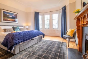 Ein Schlafzimmer mit Bett, Sessel, Kamin und Fenster.