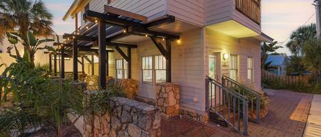 A two-story house with a stone retaining wall, a covered porch, and a staircase leading to the entrance.