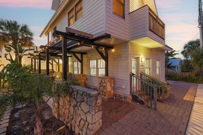 A two-story house with a stone retaining wall, a covered porch, and a staircase leading to the entrance. - 🐾 Lofty Suites: Ground Floor, Dogs Welcome + Walk Flagler Ave to Beach! (New Smyrna Beach)