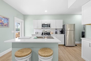 Una cocina moderna con gabinetes blancos, electrodomésticos de acero inoxidable y una isla central con taburetes.