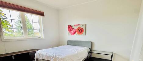 A bedroom with a bed, a ceiling fan, a window, and a painting on the wall.