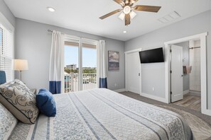 Un dormitorio con una cama grande, ventilador de techo, televisión y vista al exterior.