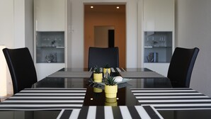 Un espace repas moderne avec une table en verre, des chemins de table rayés noirs et blancs, des chaises noires et de petites plantes en pot.