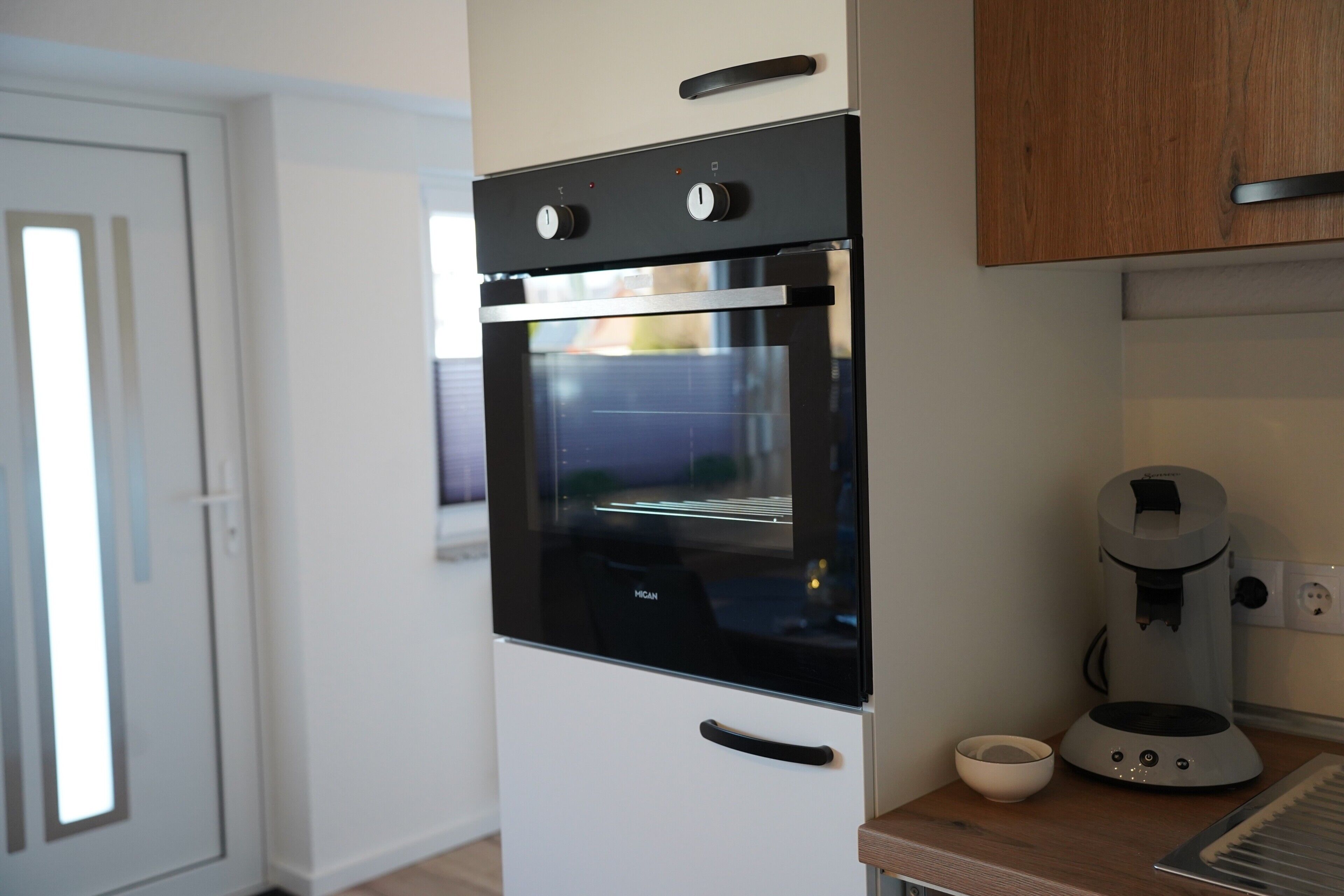 Een keuken met een zwarte oven, een koffiezetapparaat en een kom op het aanrecht.