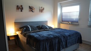 Ein Schlafzimmer mit Bett, Nachttischen, einem Fenster mit Jalousien und Wandbildern.