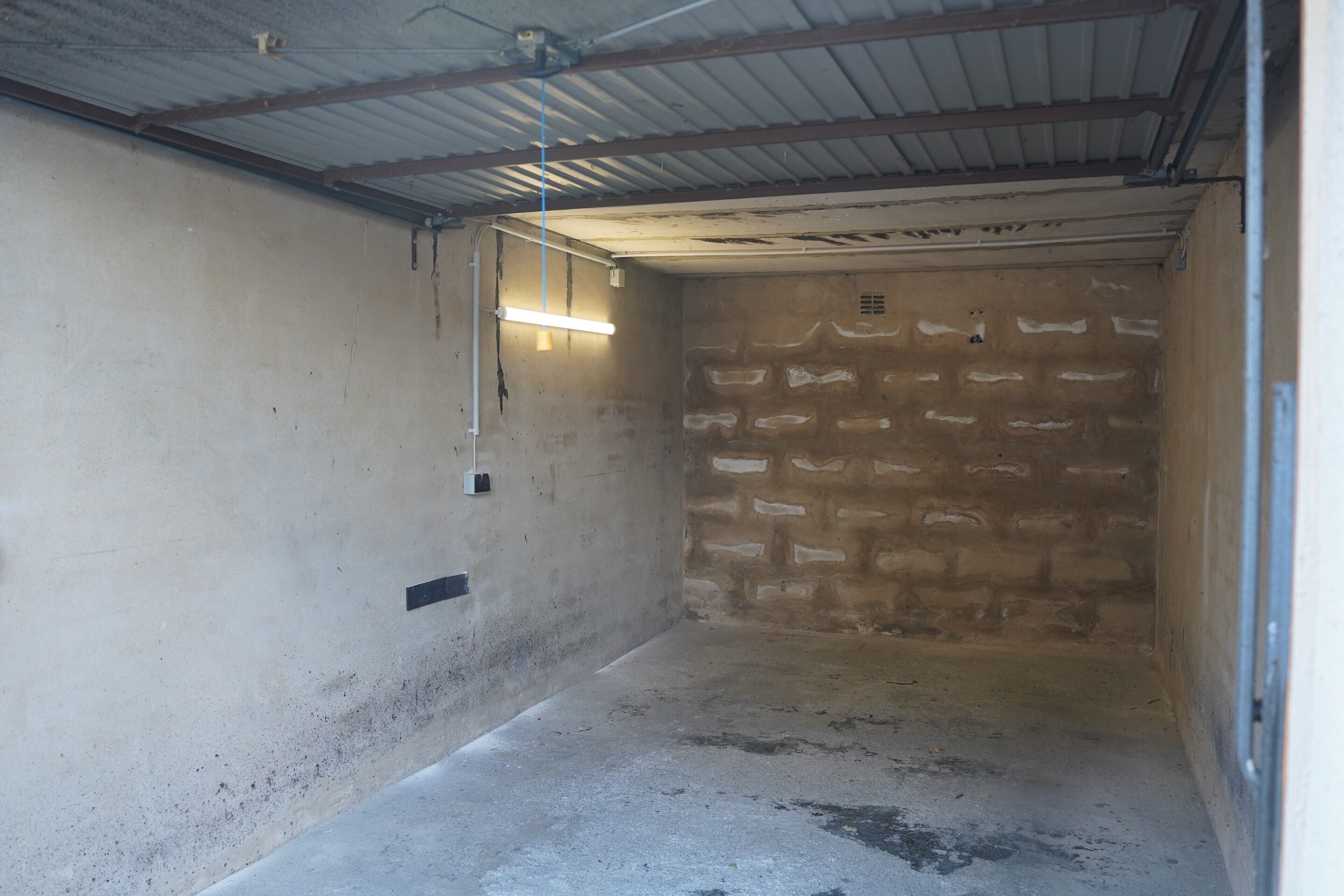 Ein mit Betonwänden ausgestatteter Raum, mit Metallverkleidung, einer Neonlampe und einem Lüftungsgitter an der Wand.