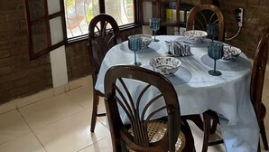 A dining area with a brick wall, a large arched window, a TV mounted on the wall, and a table set with bowls and glasses. - A place to enjoy nature 1-bedroom cabin in soothing Los Planes De Renderos. (Panchimalco)