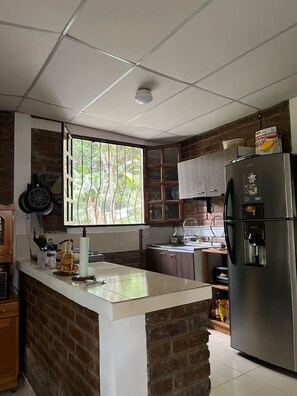 A kitchen with a brick accent wall, a stainless steel refrigerator, and a window with a view of greenery.