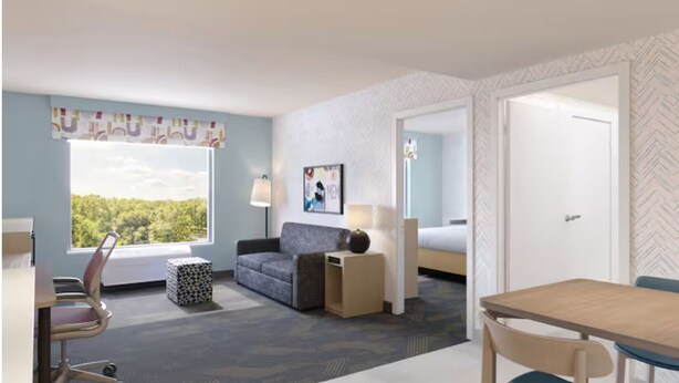 Una habitación de hotel con un ventanal grande, un sofá, una mesa, una lámpara y una cama.