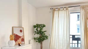 A bedroom with a bed, a dresser, a potted plant, a wall-mounted lamp, and a window with curtains.