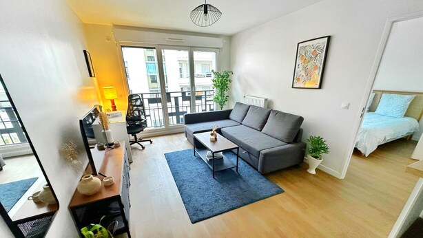 A modern living room with a sofa, coffee table, and a desk with a lamp. There is a balcony with a railing and a plant.