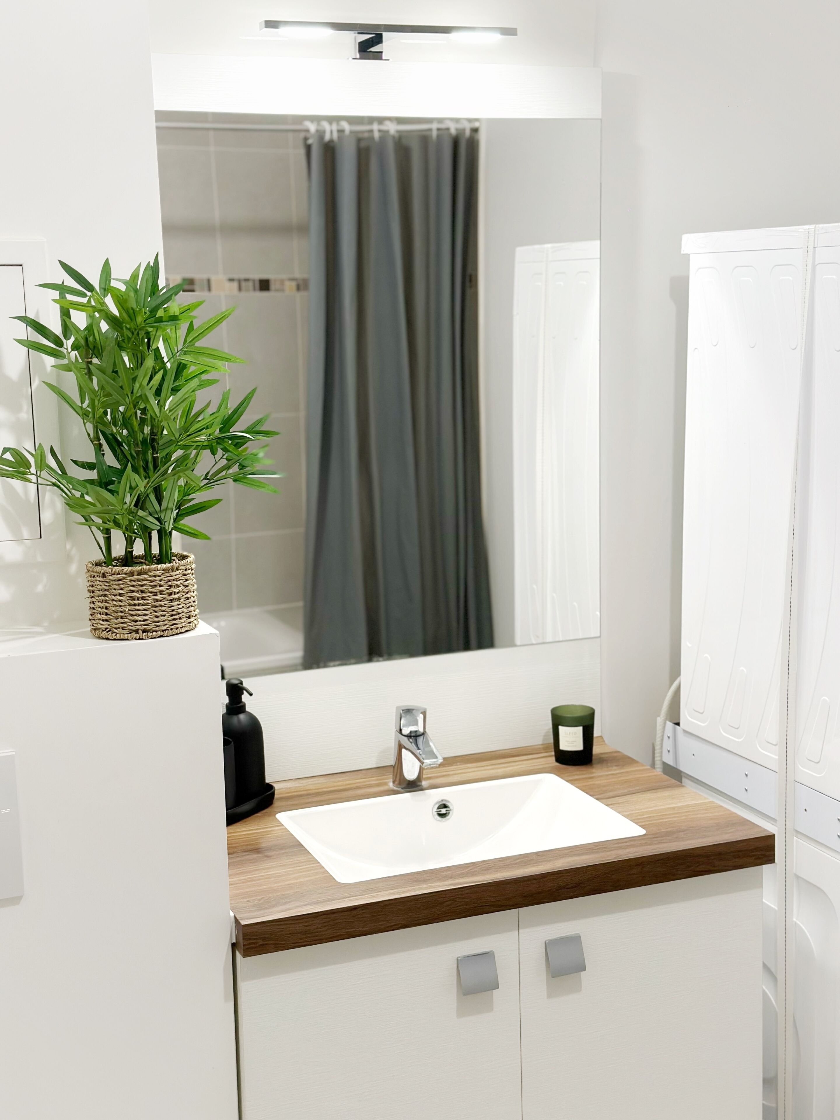 Een moderne badkamer met een witte wastafel, een houten aanrechtblad en een potplant.