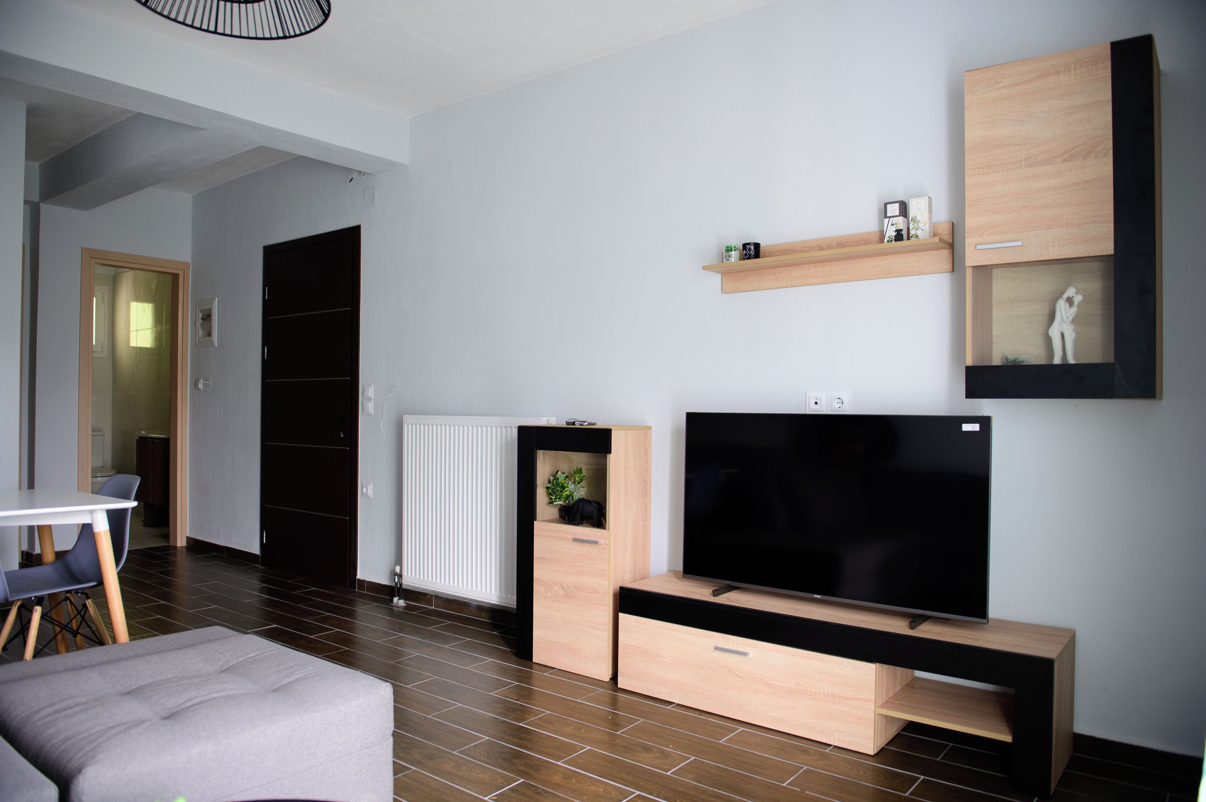 Una sala moderna con televisor de pantalla plana, armarios de madera, una zona de comedor con mesa y sillas, y un radiador.