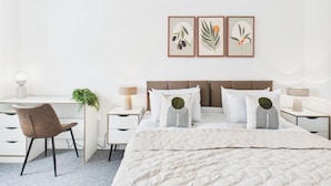 Ein Schlafzimmer mit Bett, Nachttischen, Schreibtisch, Stuhl und Wandbildern.