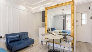 A modern room with a blue sofa, a round table with chairs, a large mirror, and a door with a window. - celine 18 (Paris)