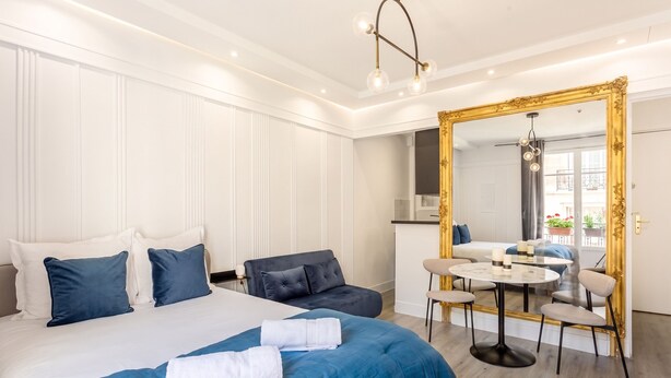 A hotel room with a large bed, a round dining table, and a mirror with a gold frame. - celine 18 (Paris)
