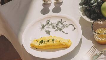 Una mesa dispuesta con un plato de comida, un bol de fruta, saleros y pimenteros, un vaso de jugo y cubiertos.
