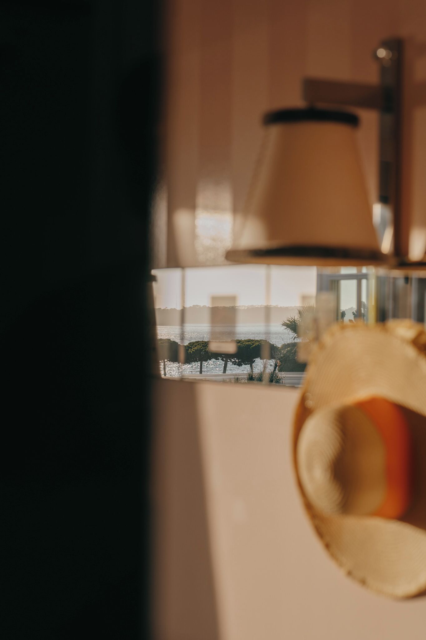 Une lampe avec un abat-jour beige, une fenêtre donnant sur la mer et une vue partielle d’un rideau.