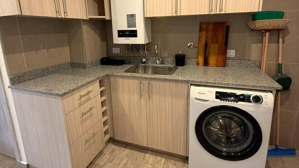A compact kitchen with wooden cabinets, a built-in washing machine, and a granite countertop. - Enjoy with your family the best view of the waterfall I Ayres del Bosque Accommodations (San Martín de los Andes)
