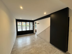 A hallway with a wooden floor, a black wall, and a door leading to a room with a stone wall and a window.
