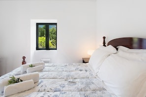 Un dormitorio con cama, ventana con vistas, mesita de noche y radiador.