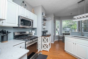 A kitchen with white cabinetry, a stainless steel stove, a microwave, and a coffee maker. - Knoxville Escape - Resort Style Backyard - Pool, Hot Tub, Sauna - Sleeps 15 (Knoxville)